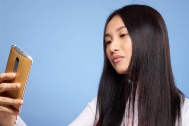 Asyalı görünümlü kadın elinde telefonla internet iletişim teknolojisi mavi arka planda.