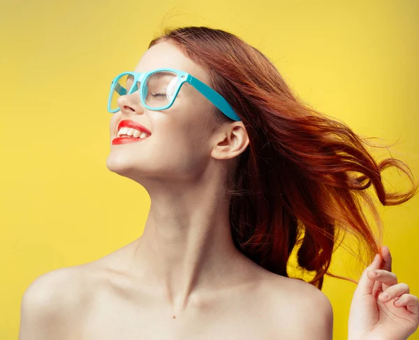 Pretty woman naked shoulders red lips blue glasses yellow background — Stock Photo, Image