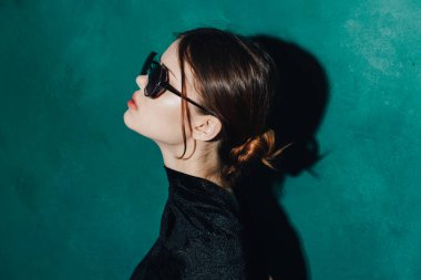 Siyah süveterli ve yeşil arka planda gözlüklü bir kadının portresi.