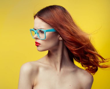 Sarı arka planda parlak makyajlı ve çıplak omuzlu neşeli bir kadın.