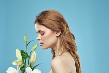 Mavi arka planda beyaz çiçeklerle dolu bir buketi olan çıplak omuzları olan güzel bir kadın.