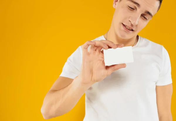 Mężczyzna w białym t-shirt pokazując kartę kredytową na żółtym tle przycięte widok — Zdjęcie stockowe