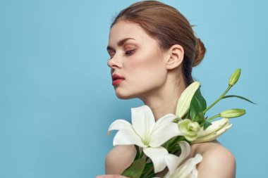 Mavi arka planda bir buket beyaz çiçekli güzel bir kız çıplak omuz portresi.