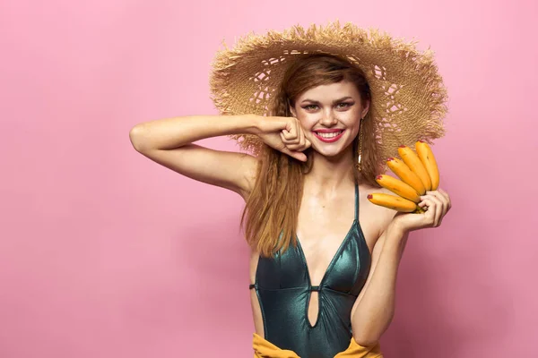 Mulher na praia chapéu de palha bananas segurando frutas Fato de banho exótico fundo rosa — Fotografia de Stock