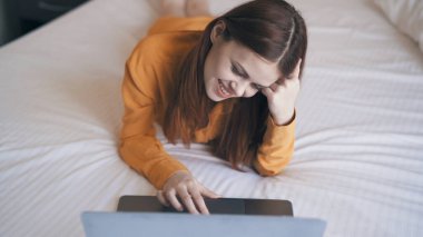 Yatak odasındaki kadın dizüstü bilgisayarlı iletişim teknolojisiyle yatakta uzanıyor.