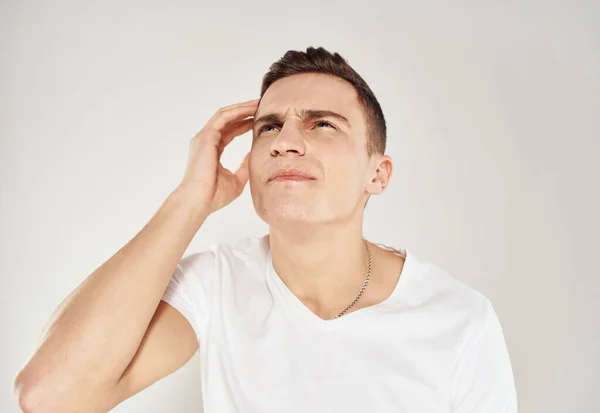 Homem pensativo em uma camiseta branca toca seu rosto com a mão em um retrato de fundo claro de um modelo — Fotografia de Stock