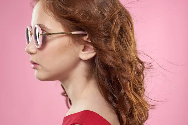 Дівчина з кучерявим волоссям темні круглі окуляри весела червона сукня рожевий фон — стокове фото