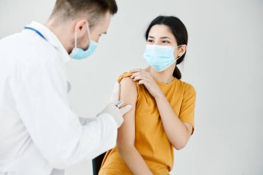 Doktor, sarı tişörtlü bir kadının omzuna yakın plan kovan aşısı enjekte ediyor.