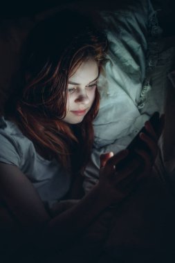 Geceleri elinde telefon olan bir kadın yatmadan önce dinleniyor.