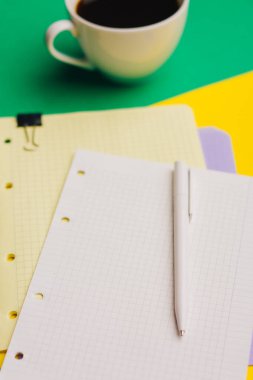 Renkli arka planda bir fincan kahve ve kağıt not defteri ofis bardakları.