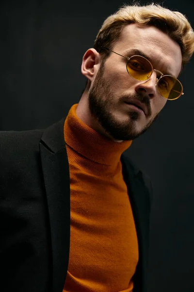 Snygg man i gula glasögon och en orange tröja böjd över till sidan mot en mörk bakgrund — Stockfoto