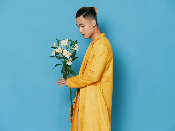 Vista lateral de um homem em um casaco amarelo com um buquê de flores em um fundo azul — Fotografia de Stock