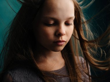 Gri elbiseli, turkuaz arka planda dağınık saçlı üzgün kız.