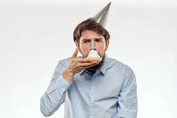 Un hombre celebra un cumpleaños sobre un fondo claro con un pastel en un plato gorra divertida flauta — Foto de Stock