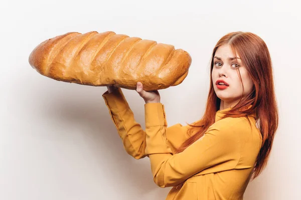 Mulher em uma camisa amarela com um enorme pão em suas mãos um produto de farinha luz fundo — Fotografia de Stock