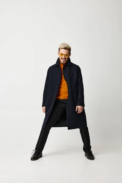 Модный мужчина в пальто раздвинул ноги на светлом фоне и оранжевый свитер брюки туфли — стоковое фото