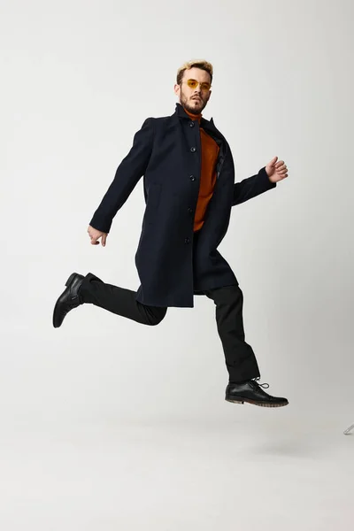 A blond man in a coat jumped up and runs to the side on a light background — Stock Photo, Image
