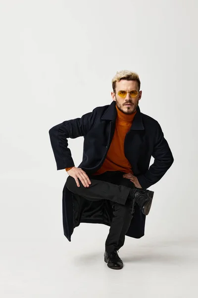 Een blonde man in bril en modieuze kleding zit op een been en zwarte laarzen — Stockfoto