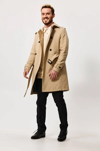 Lindo chico en abrigo beige y pantalones va a un lado en un fondo claro y traje de estilo de moda — Foto de Stock