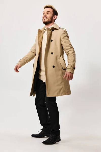 Un hombre en un abrigo beige y pantalones en un fondo ligero botas Copiar espacio — Foto de Stock