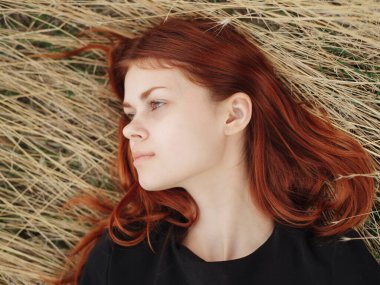 Siyah elbiseli bir kadın doğadaki bir çayırda kuru çimenlerin üzerinde yatıyor.