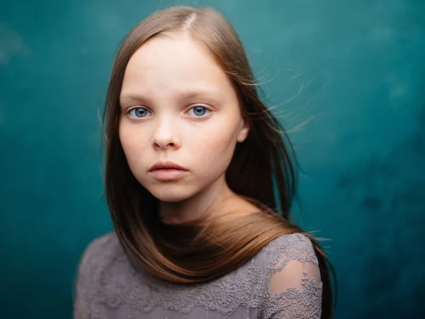 Portret van een mooi meisje in een grijze jurk en blond haar op een turquoise achtergrond — Stockfoto