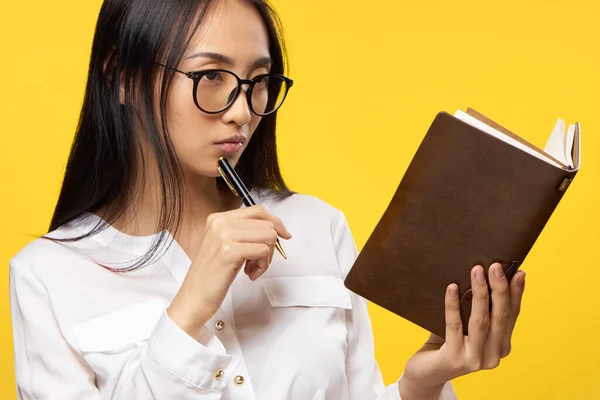 Žena asijského vzhledu při pohledu na poznámkový blok pero v ruce oficiální žluté pozadí — Stock fotografie