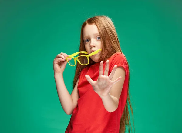 Έκπληκτη κοπέλα με κόκκινα μαλλιά κρατώντας γυαλιά στα χέρια της συναισθήματα πράσινο σχολείο φόντο — Φωτογραφία Αρχείου