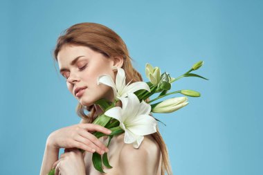 Mavi arka planda güzel bir kadın çıplak omuzunda bir buket beyaz çiçekle