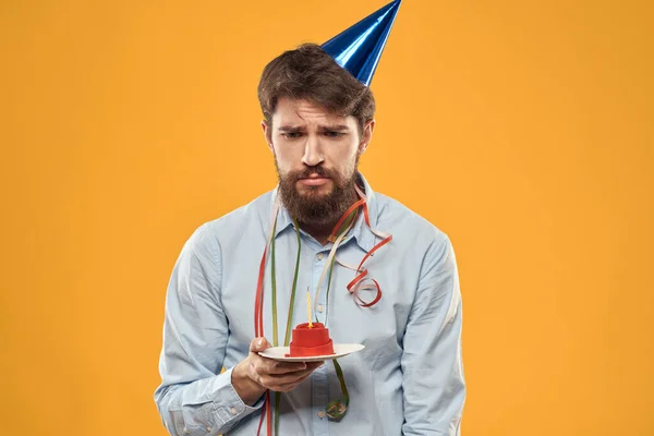 Cheerful man with a cake on a yellow background birthday holidays cap on his head