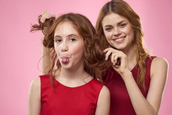 Mãe e filha em vestidos vermelhos abraços diversão grimace infância alegria rosa fundo — Fotografia de Stock