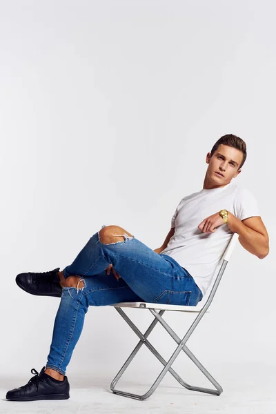 一个穿着牛仔裤和T恤衫的男人坐在椅子上，背景色轻盈 — 图库照片