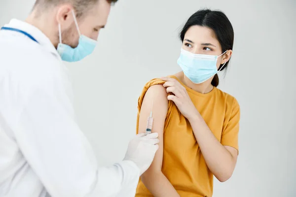 En läkare i vit rock injicerar ett vaccin i axeln på en kvinna i en medicinsk mask — Stockfoto