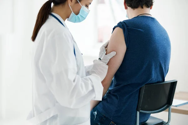 Kvinna läkare i en medicinsk mask injicera en man i en blå t-shirt covid vaccination — Stockfoto