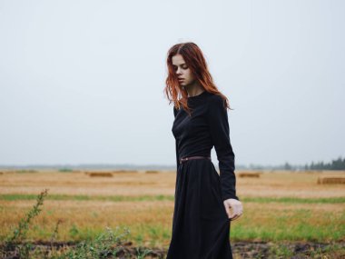 Siyah elbiseli bir kadın akşam modeliyle doğa üzerinde yürüyor.