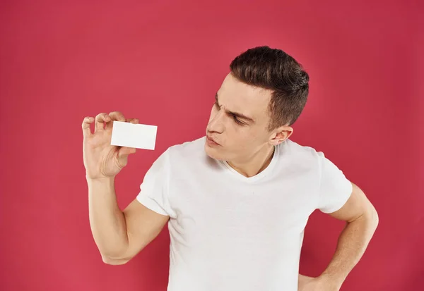 Працівник з кредитною карткою на червоному тлі та білою футболкою обрізаний вид — стокове фото