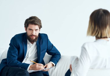 Klasik takım elbiseli bir adam kanepede oturuyor. Elinde belgeler ve boş bir kadın var.