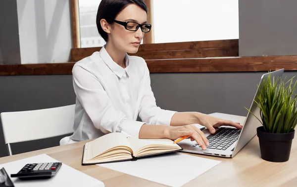 Frau arbeitet hinter Laptop im Büro und Notizblock auf dem Tisch — Stockfoto