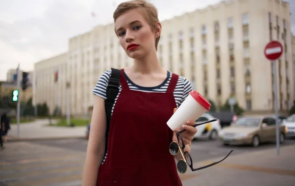 A woman in a sundress walks down the street with a cup of coffee in her hand — Stock Photo, Image