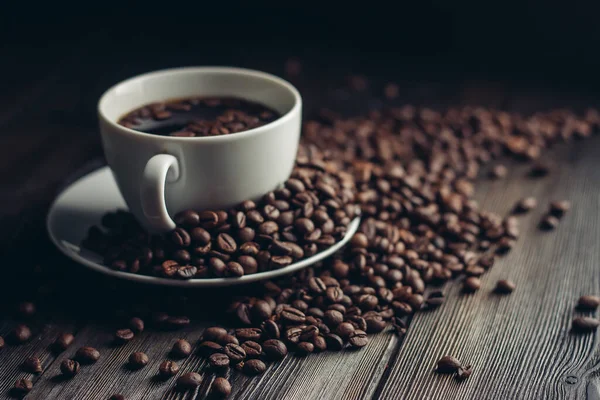 Granos de café fragantes en una mesa de madera y una taza con una bebida caliente en un platillo — Foto de Stock