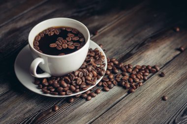 Kahve çekirdekli çay tabağı ve ahşap masa manzaralı beyaz bardak. Boşluğu kopyala.