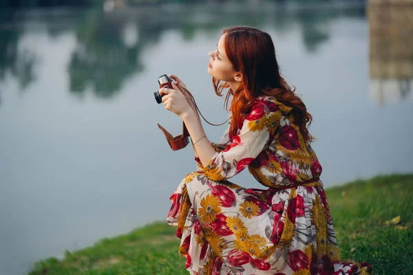 Рыжая женщина с камерой на природе возле озера — стоковое фото