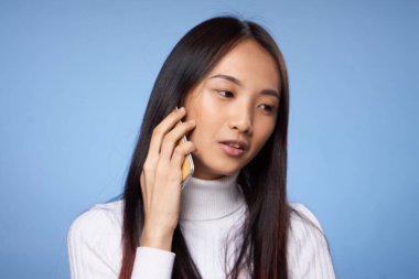 Koreli kadın mavi arka planda cep telefonuyla konuşuyor