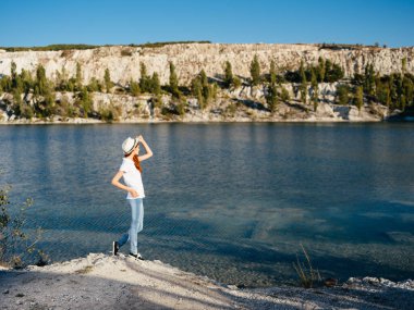 Doğada şeffaf bir nehrin kenarında elinde şapkası olan mutlu bir kadın.