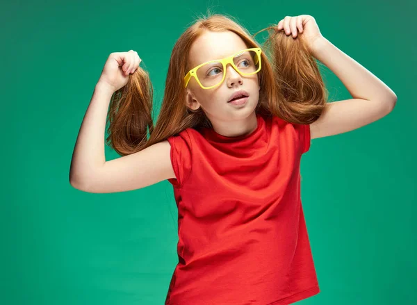 Lány egy piros póló laza haj érzelmek sárga szemüveg Zöld háttér — Stock Fotó