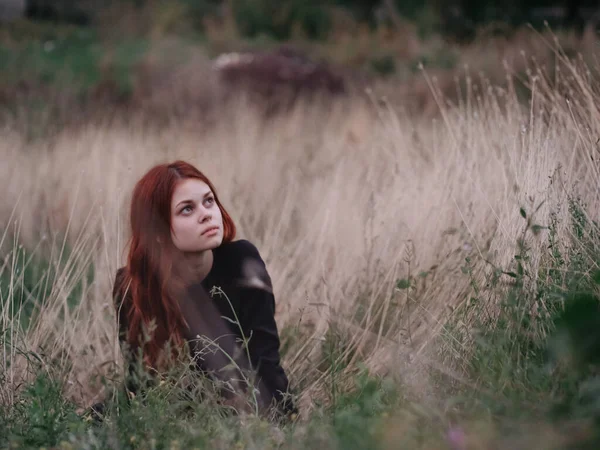 Red-haired woman in a black dress lies in a field on dry grass in nature — Stock Photo, Image