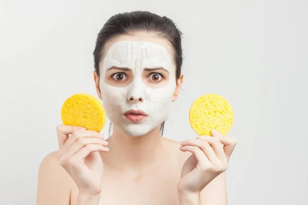 Mujer con hombros desnudos limpia una máscara en su cara con esponjas — Foto de Stock