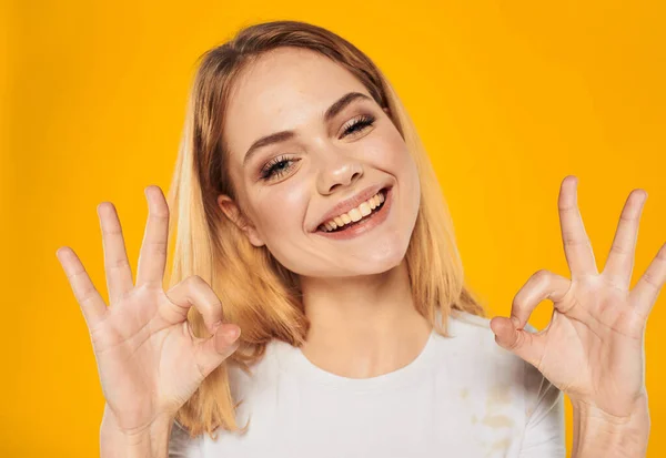 Mujer feliz deleite emociones alegría rubia sobre un fondo amarillo gestos con las manos —  Fotos de Stock