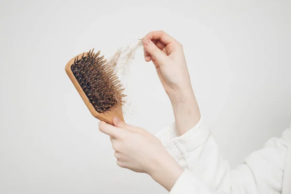 Mulher remove um pão de cabelo com um pente de madeira em um fundo leve perda de problemas de saúde — Fotografia de Stock