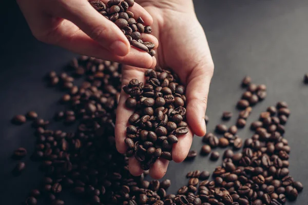 Granos de café en manos esparcidas sobre un fondo oscuro — Foto de Stock